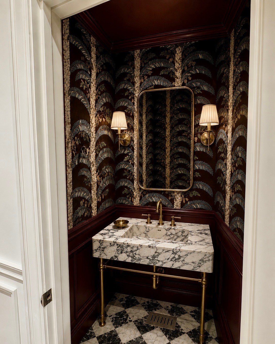 Tiny powder room with palm wallpaper carried over the ceiling, oxblood lacquered panelling and a marble basin on brass legs